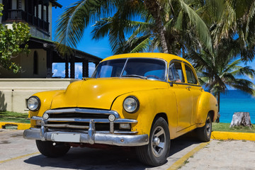 Gelber amerikanischer Oldtimer parkt unter Palmen am Strand in Varadero Kuba - Serie Kuba Reportage