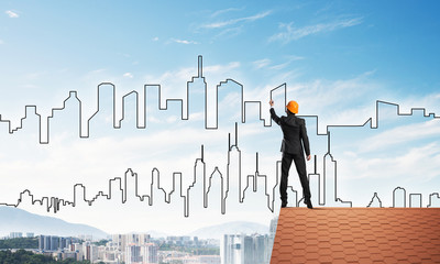 Man architect draw silhouette of modern city on blue sky. Mixed media