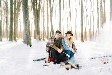 Fototapeta na wymiar stylishly dressed young couple, sitting near the fire in the winter forest