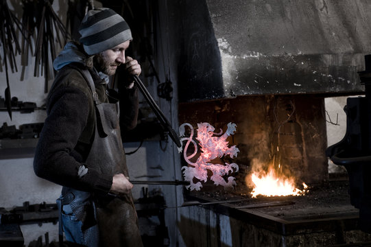 Blacksmith making coat of arms from iron, forge in background, Landshut, Bavaria, Germany