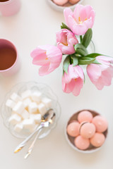 Naklejka na ściany i meble Spring background. Sweets and tea on a table with pink tulips. Still life with fresh bouquet of tulips. Beautifully decorated tray.