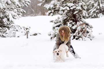 Funny girl with golden retriever labrador in winter forest. Friendship, pet and human.