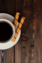 cup and chocolate tube on a saucer, wooden background