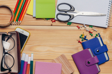 Stationery on a wooden background, a bag with glasses and a phone