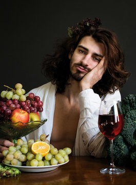 photo half naked curly drunk guy at a table with fruits and wine
