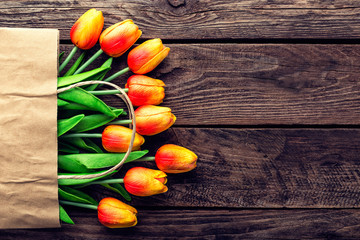 Bouquet of tulips in a paper shopping bag on a wooden background, concept of discounts and sales on the Women's Day or Mother's Day or Easter