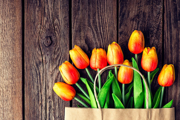 Bouquet of tulips in a paper shopping bag on a wooden background, concept of discounts and sales on the Women's Day or Mother's Day or Easter