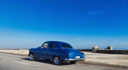 Obraz na płótnie Canvas Blauer amerikanischer Oldtimer fährt auf dem Malecon im Hintergrund die karibische See in Havanna Kuba - Serie Kuba Reportage