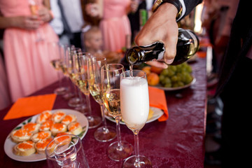 Bartender pours champagne from bottle to glasses at reception