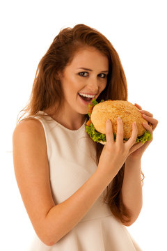 Unhealthy meal - happy young woman eats hamburger isolated over white