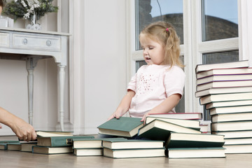 Little girl sits on the floor and play. Portrait of child has pile of books.