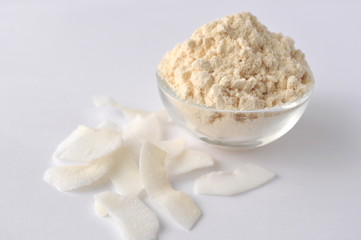 Coconut flour and flakes on white background. Cream powder in a glass bowl. Isolated on white. Alternative gluten-free flour for baking and cooking
