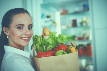 Young woman holding grocery shopping bag with vegetables .Standing in the kitchen