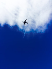 Silhouette of a plane against white clouds and a blue sky. - 137621458