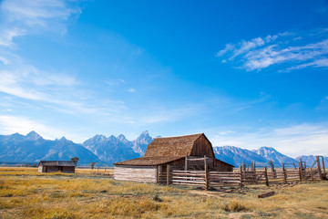 Grand Teton National Park, Jackson Hole, Wyoming.  Barn in a grass field plain against the Grand Teton mountain range with the sun shining