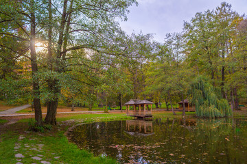 Autumn park with pond and wooden alcoves.