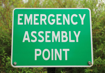 green and white Emergency Assembly Point sign with blurred background