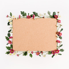 Frame with red and white wildflowers, green leaves, branches and wooden cork tree board on white background. Flat lay, top view. Flower background.