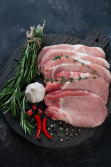 Wooden cutting board with raw seasoned pork chop steaks