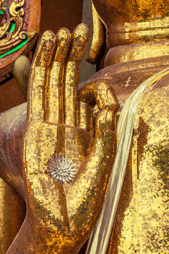 A hand of buddha statue made from many small pieces of square yellow glass.