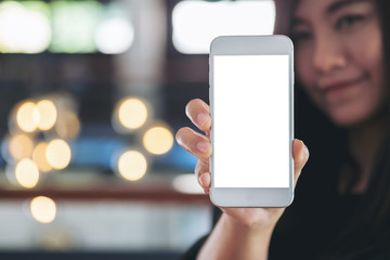 Mockup image of a beautiful woman holding and showing white mobile phone with blank black screen and smiley face in vintage cafe