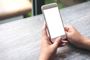 Mockup image of hands holding white mobile phone with blank white screen on vintage wooden table