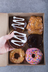 A box with six donuts. A hand holding a chocolate frosted donut. 