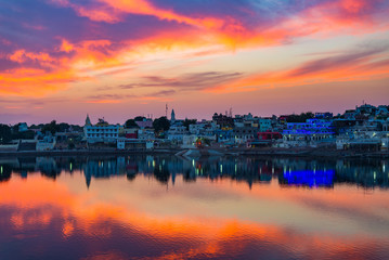 Fototapeta na wymiar Colorful sky and clouds over Pushkar, Rajasthan, India. Temples, buildings and colors reflecting on the holy water of the lake at sunset.