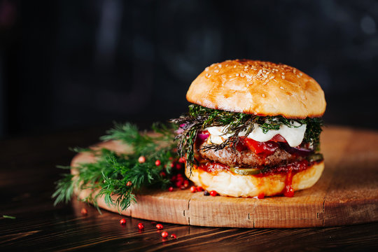 Burger with  meat, tomato, dill and cheese sauce on wooden background. Close up. Copy space