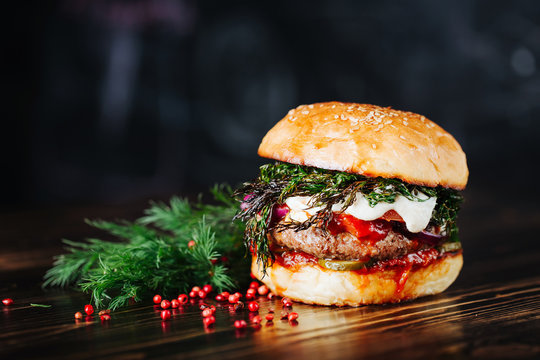 Burger with meat, tomato, dill and cheese sauce on wooden black background. Close up. Copy space. Decoration with red bell pepper