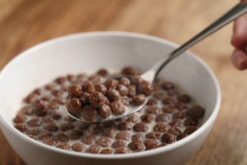 eating with spoon chocolate cereal balls with milk in white bowl for breakfast on wooden table
