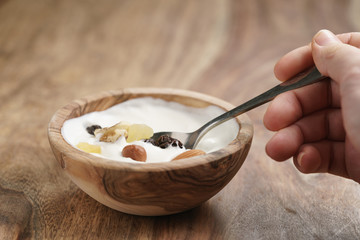 eating with spoon homemade yogurt with muesli in wood bowl on wooden table