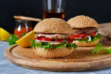 Big homemade burger with meat, tomato and sauce on a cutting board. Concrete background. Fast food.