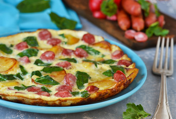 Omelet with spinach, cheese and Bavarian sausages on a concrete background