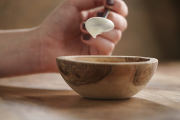 eating with spoon homemade organic yogurt in wooden bowl on table