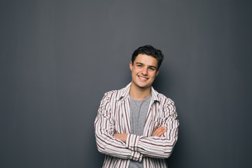 Happy cheerful guy with crossed hands on gray background