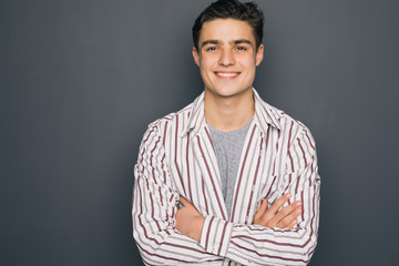 Happy cheerful guy with crossed hands on gray background