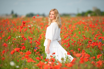 Fototapeta na wymiar smiling young woman in white dress in the blooming red poppy field