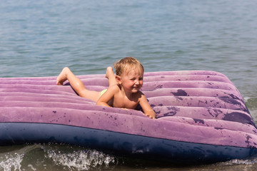 Baby floats on inflatable mattress in the sea