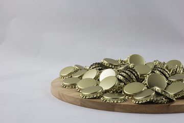 Pile of bottle caps on a wooden tray with white background.