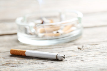 Cigarette with ash on grey wooden table