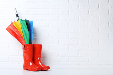 Red rubber boots with umbrella on brick wall background