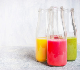 Fototapeta na wymiar Bottles with colorful drinks: smoothies or juices on light background, front view