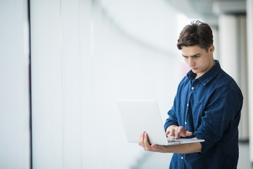 Handsome young man man holding a laptop in hall