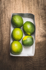 Fresh green lime in paper box on rustic wooden background, top view