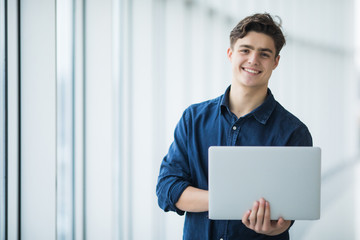 Handsome young man man holding a laptop in hall