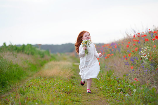 Charming red-haired girl running with a bouquet of daisies