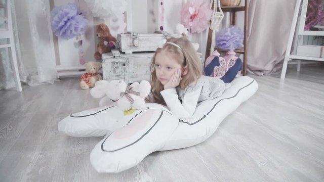 Little cute girl playing with plush toys and lays on the big soft toy hare. Children's imaginations: play with toys. Little girl in teepee tent. Wigwam for children in a room.