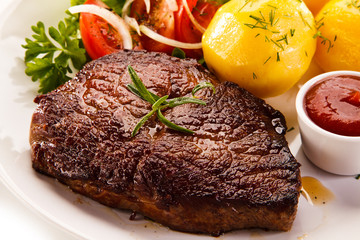Grilled steaks, boiled potatoes and vegetable salad on white background 