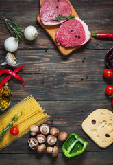 Raw beef steak with pasta, tomatoes, mushrooms and cheese on dark table background, top view. copyspace